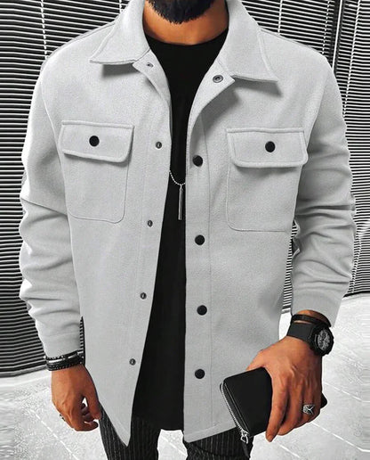 Jules | Chemise oversize pour homme à manches longues, couleur blanche, avec poches à rabat et boutons noirs, portée avec un t-shirt noir et un pantalon à rayures.