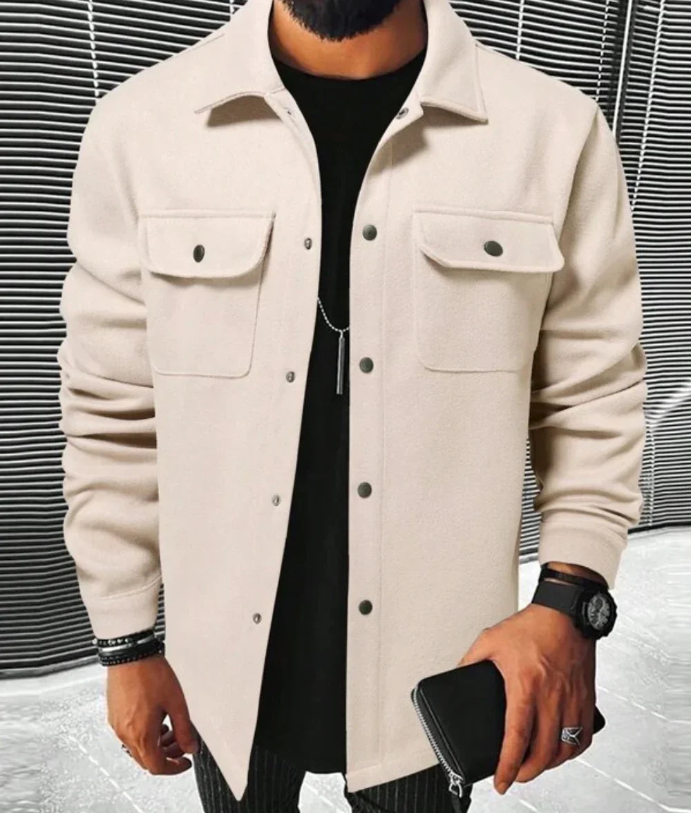 Jules | Chemise oversize pour homme à manches longues, couleur beige, avec poches à rabat, fermée par des boutons noirs, portée avec un t-shirt noir et un pantalon à rayures.