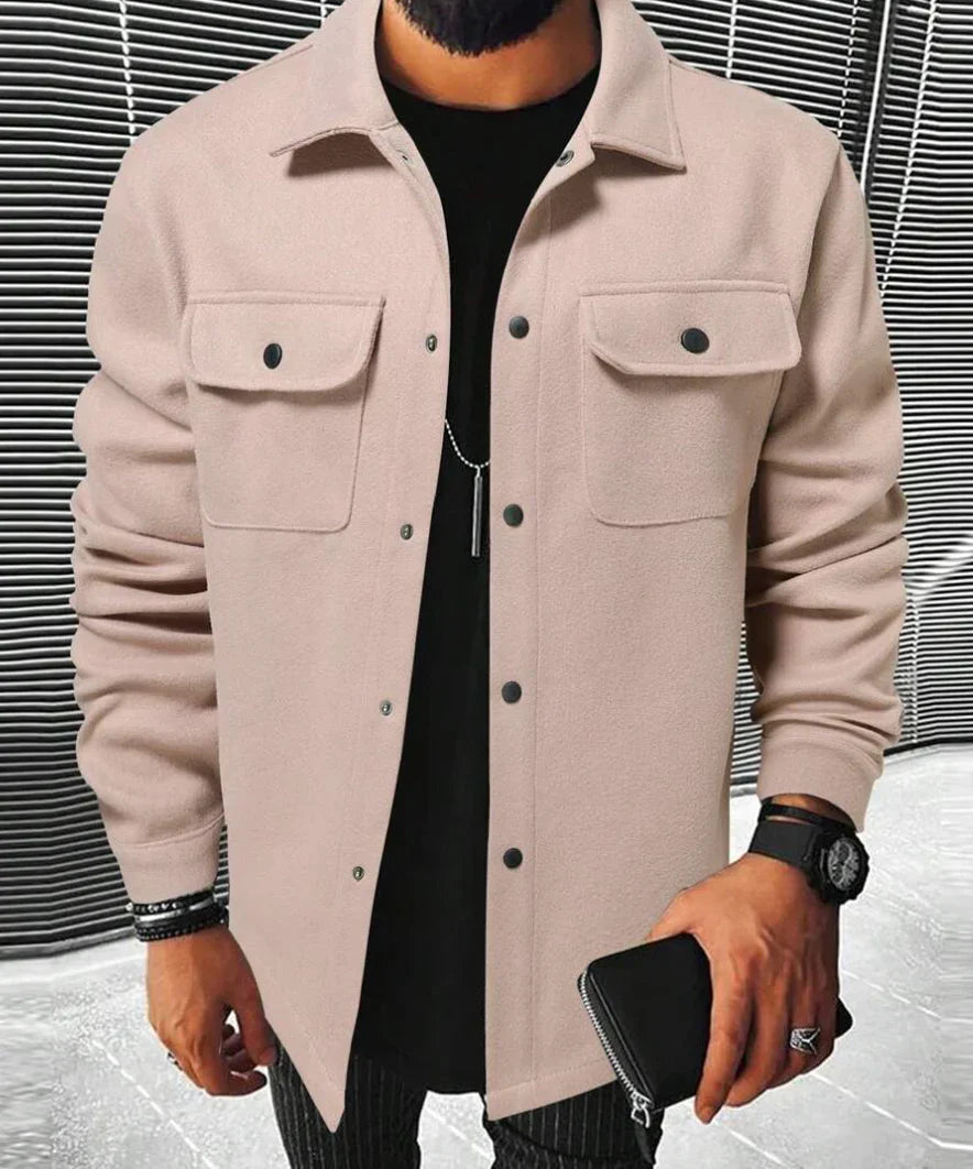 Jules | Chemise oversize pour homme, à manches longues, de couleur rose pâle avec poches poitrine et boutons noirs, portée avec un t-shirt noir et un pantalon à rayures.