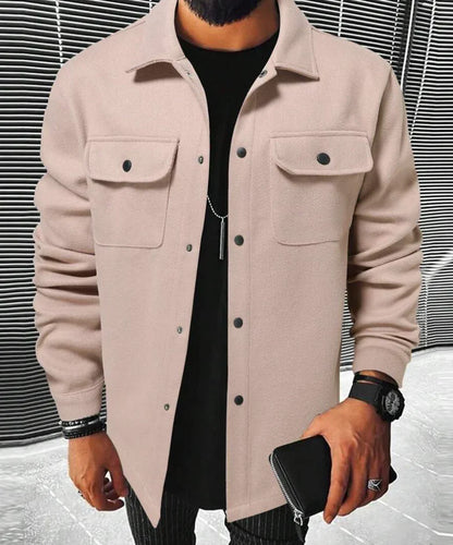 Jules | Chemise oversize pour homme, à manches longues, de couleur rose pâle avec poches poitrine et boutons noirs, portée avec un t-shirt noir et un pantalon à rayures.