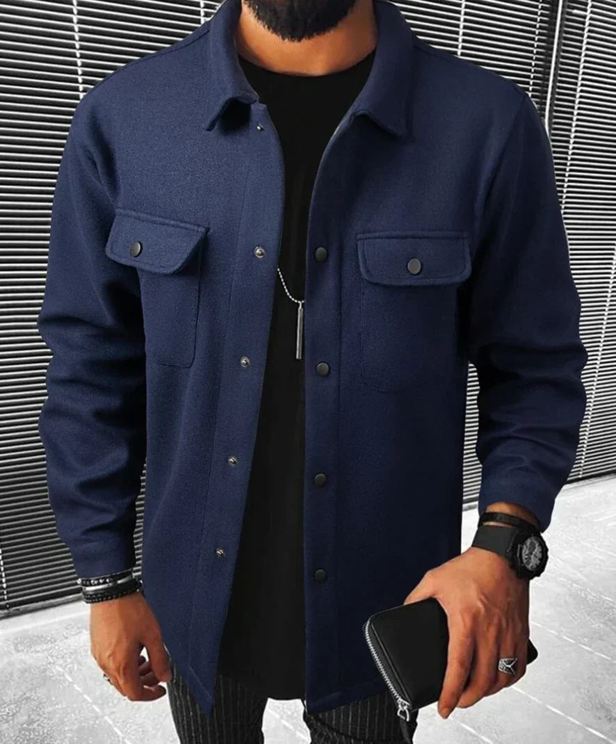 Jules | Chemise oversize pour homme, à manches longues, de couleur bleue, avec poches à rabat et boutons noirs, portée avec un t-shirt noir et un pantalon à rayures.