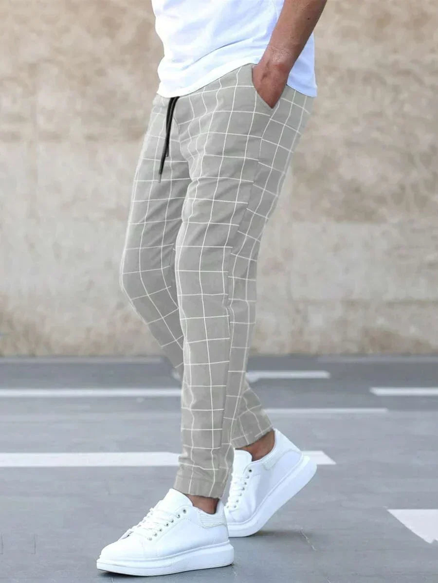 Homme portant le pantalon classique Juste pour hommes, beige clair à carreaux, coupe ajustée avec chevilles resserrées, poches latérales et cordon de serrage, associé à un t-shirt blanc et des baskets blanches  style tendance et confortable.