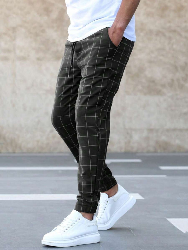 Homme portant le pantalon classique Juste pour hommes, noir à carreaux, coupe slim avec chevilles resserrées, poches latérales et cordon de serrage, porté avec un t-shirt blanc et des baskets blanches look tendance et chic.