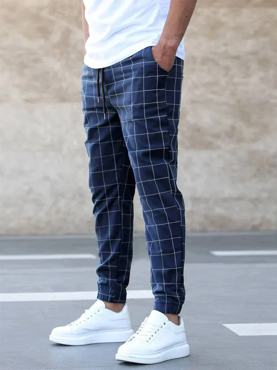 Pantalon classique pour homme Juste bleu marine à carreaux, coupe tendance ajustée avec cordon de serrage et chevilles resserrées, porté avec t-shirt blanc et baskets blanches.
