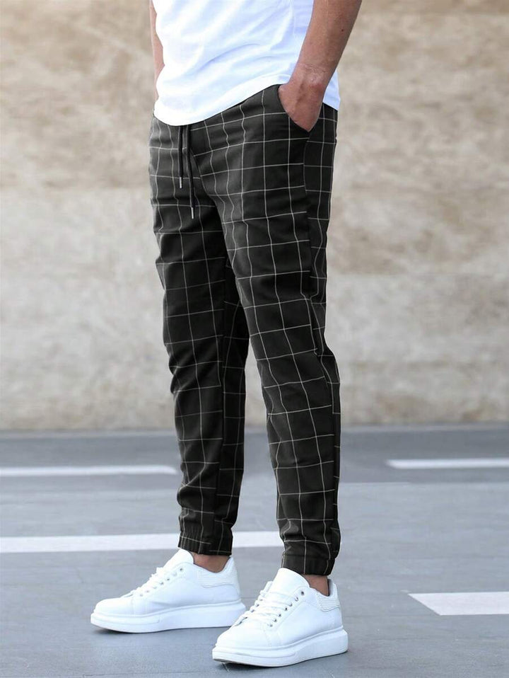 Pantalon classique pour homme Juste kaki foncé à carreaux, coupe tendance ajustée avec cordon de serrage, porté avec t-shirt blanc et baskets blanches.