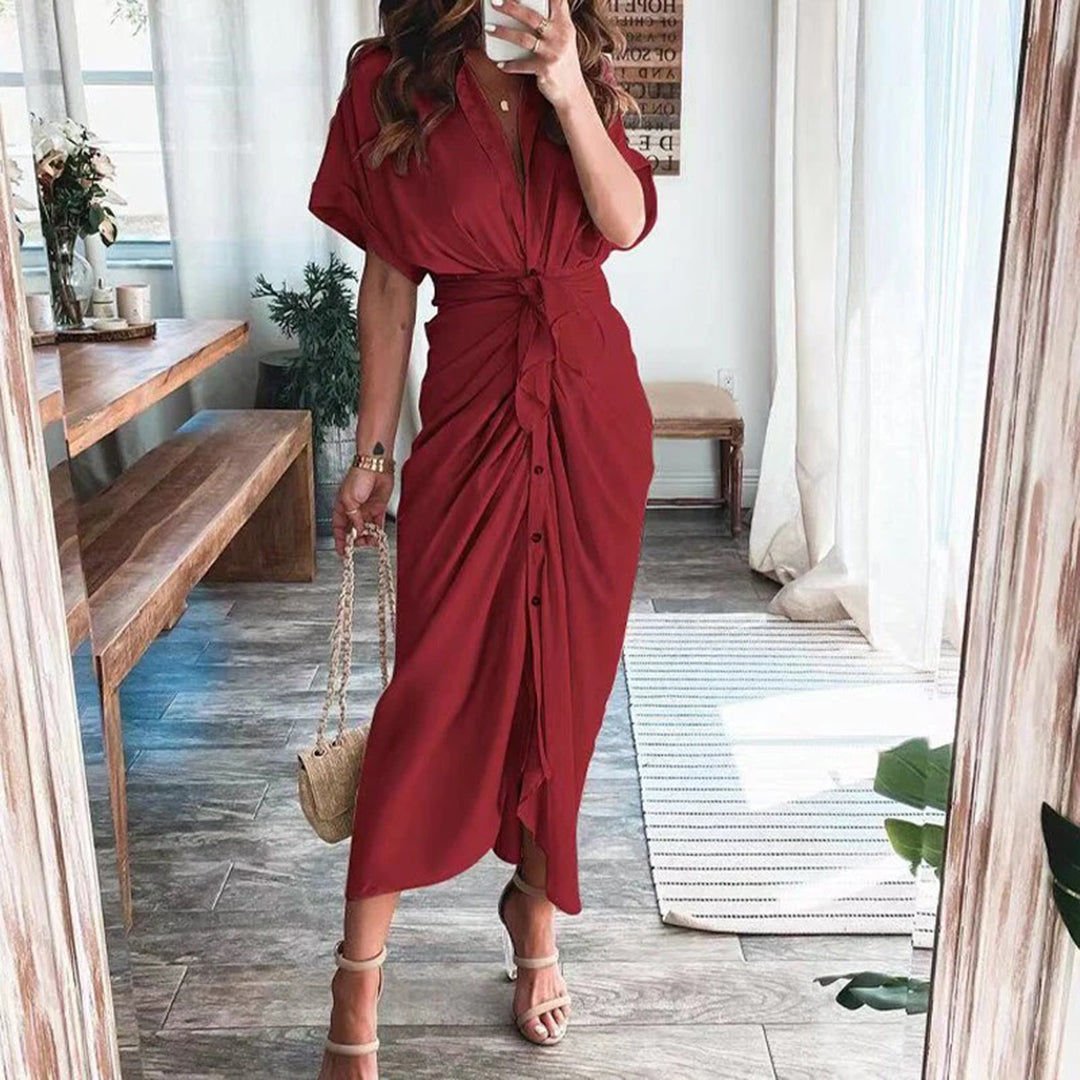 Robe midi rouge élégante avec une coupe fluide et une taille nouée, mettant en valeur la silhouette. Les boutons sur le devant apportent une touche chic et moderne, tandis que les sandales à talons et le sac à main complètent ce look sophistiqué, parfait pour les occasions spéciales.