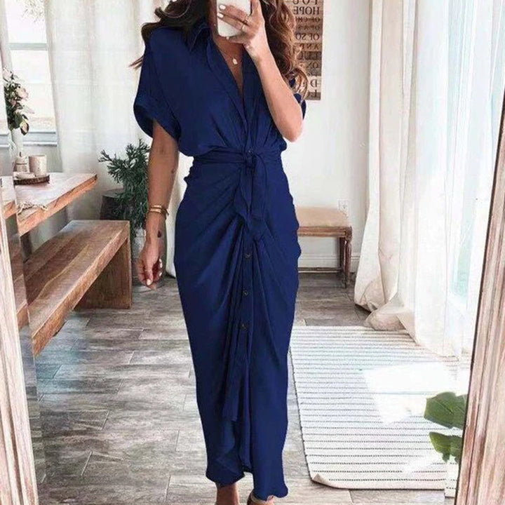 Robe midi bleu marine avec une coupe fluide et un détail noué à la taille. Les boutons sur le devant ajoutent un accent élégant, tandis que les talons et l'intérieur lumineux créent un look chic et moderne, idéal pour des occasions décontractées ou élégantes.