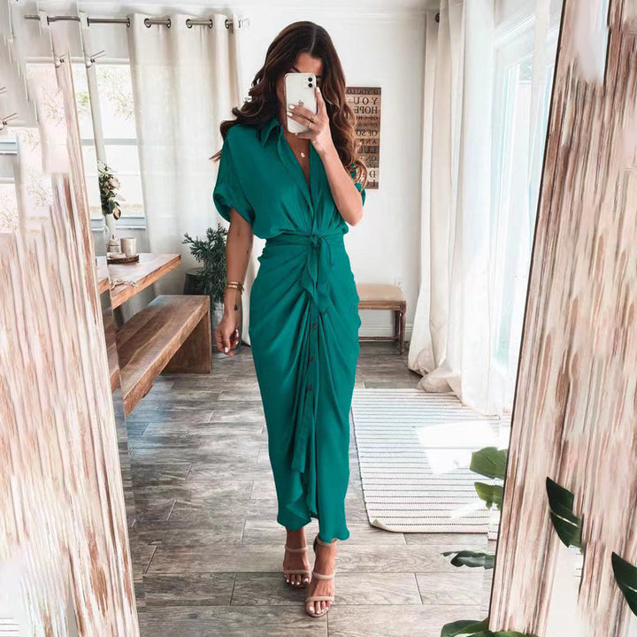Robe midi verte avec une coupe fluide et une taille nouée, créant une silhouette élégante. Les boutons sur le devant ajoutent un détail chic, tandis que les talons et l'environnement lumineux ajoutent une touche moderne et sophistiquée, parfaite pour des occasions ou des sorties stylées.