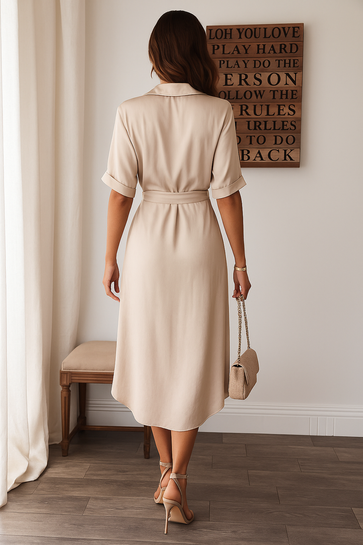 Vue arrière d'une élégante robe midi beige avec une coupe fluide et un ceinturage à la taille. La robe est accompagnée d'une pochette et de talons hauts, créant un look chic et moderne, parfait pour des occasions formelles ou des sorties élégantes.