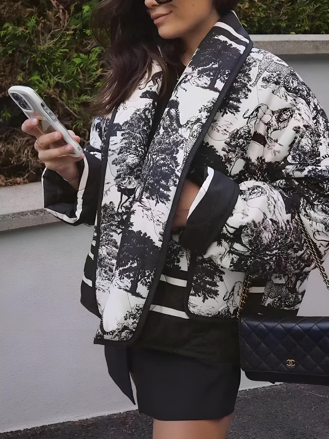 Veste courte d’hiver pour femme Kérina, à motif noir et blanc élégant, portée avec une jupe noire. La veste au style chic et moderne est associée à un sac matelassé et parfaite pour une tenue urbaine sophistiquée.