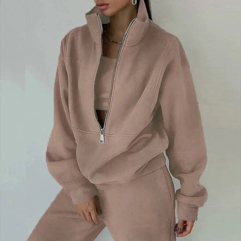 Une femme porte un ensemble décontracté de couleur beige, composé d'un haut à col zippé et d'un pantalon assorti. Le style décontracté est parfait pour les journées d'hiver, offrant confort et élégance.