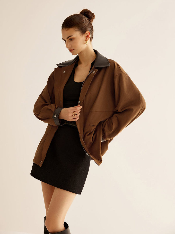 Veste oversize Kylora pour femme, avec un col en cuir noir et une coupe décontractée. Cette veste tendance est parfaite pour un look chic et moderne, associée à une mini-jupe noire et des bottes, créant une silhouette élégante et contemporaine.