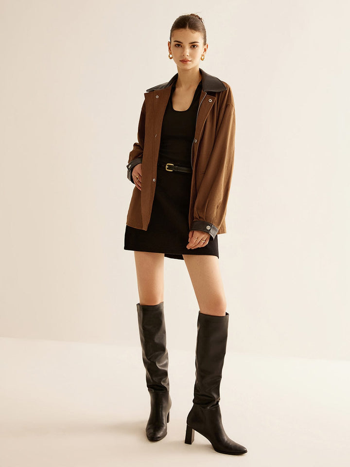 Veste oversize Kylora pour femme, combinant un style moderne et tendance. Le modèle porte la veste avec une mini-jupe noire et des bottes hautes en cuir, créant un look chic et audacieux. Le col en cuir noir ajoute une touche sophistiquée à l'ensemble.