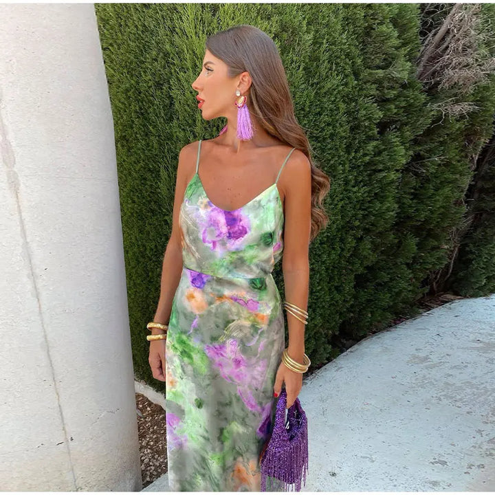 Robe maxi de soirée Kyra pour femme, élégante et fluide, à fines bretelles avec imprimé artistique vert, violet et touches pastel. Coupe légère et féminine, parfaite pour un look chic et tendance, accessoirisée avec bijoux dorés et pochette violette.