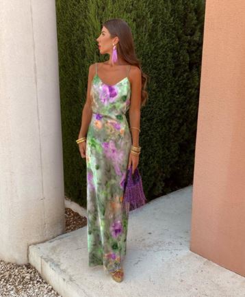 Robe maxi de soirée Kyra pour femme, fluide et élégante, à imprimé floral pastel vert et violet, avec fines bretelles et coupe légère. Portée avec des accessoires dorés et une pochette violette, idéale pour une allure chic et tendance lors d’événements estivaux.