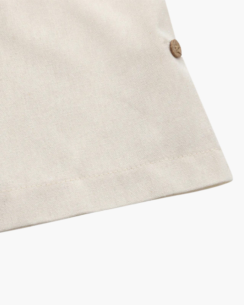 Zoom sur le bas du polo en lin pour homme, couleur beige clair, avec un bouton en bois décoratif qui ajoute un détail élégant à la coupe droite. Un design simple et raffiné pour un style à la fois décontracté et chic.