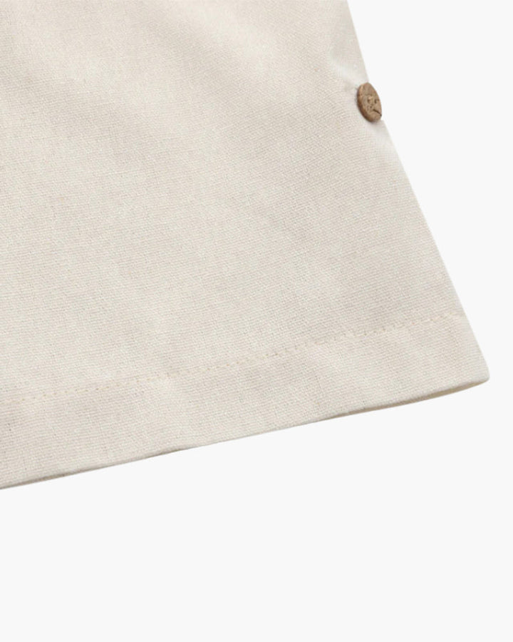 Zoom sur le bas du polo en lin pour homme, couleur beige clair, avec un bouton en bois décoratif qui ajoute un détail élégant à la coupe droite. Un design simple et raffiné pour un style à la fois décontracté et chic.