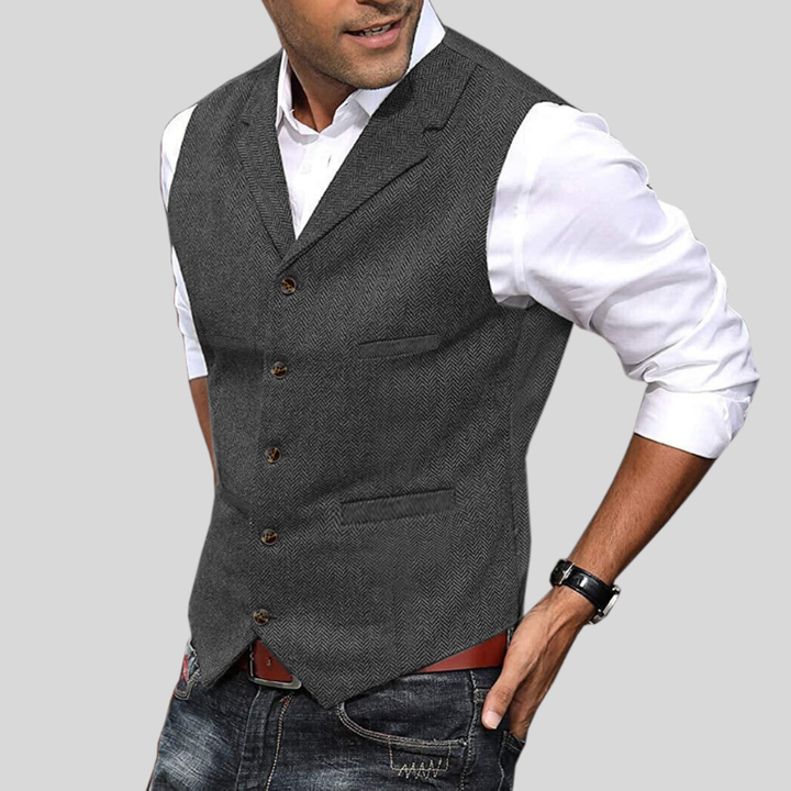 Gilet court sans manches gris à boutons, coupe ajustée avec poches, porté sur une chemise blanche avec jean.