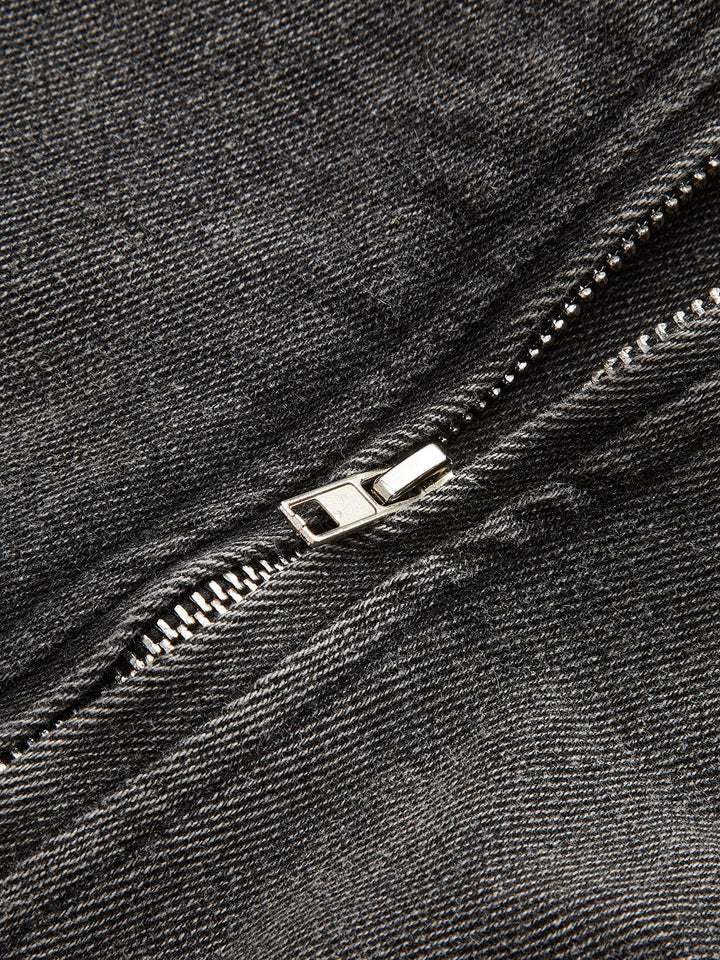 Gros plan sur le détail de la fermeture zippée en métal argenté sur denim gris délavé, mettant en valeur la finition soignée et le style moderne de la veste.