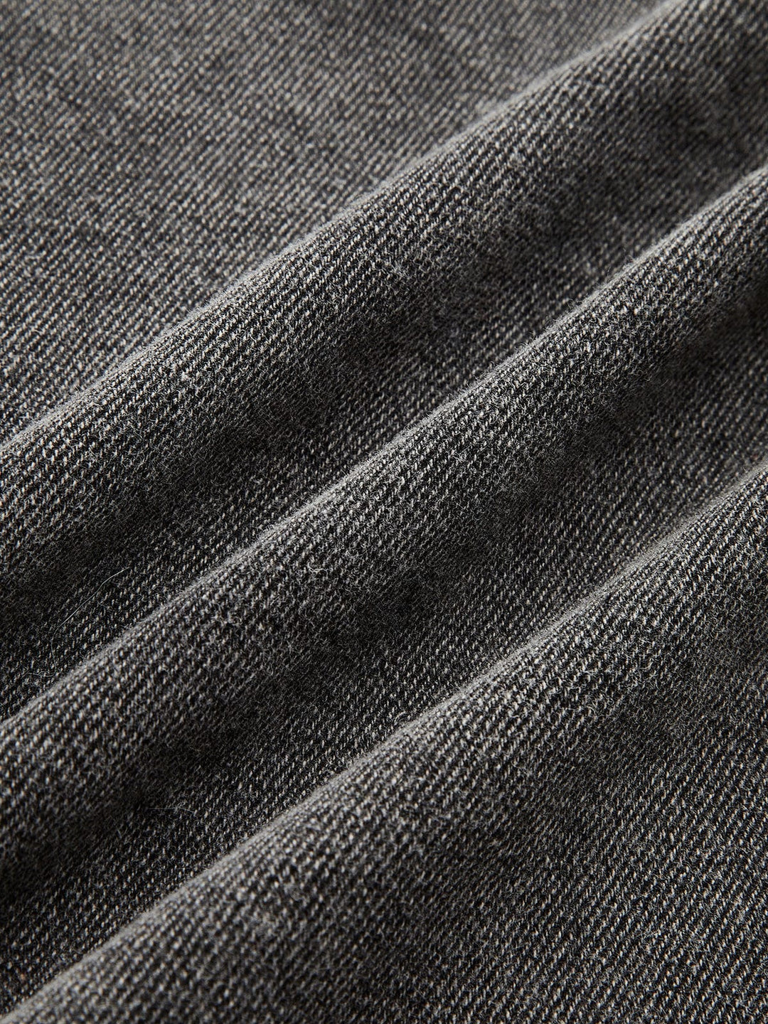 Gros plan sur le tissu en denim gris délavé, mettant en évidence la texture résistante, le tissage serré et la qualité du matériau pour un style moderne et durable.