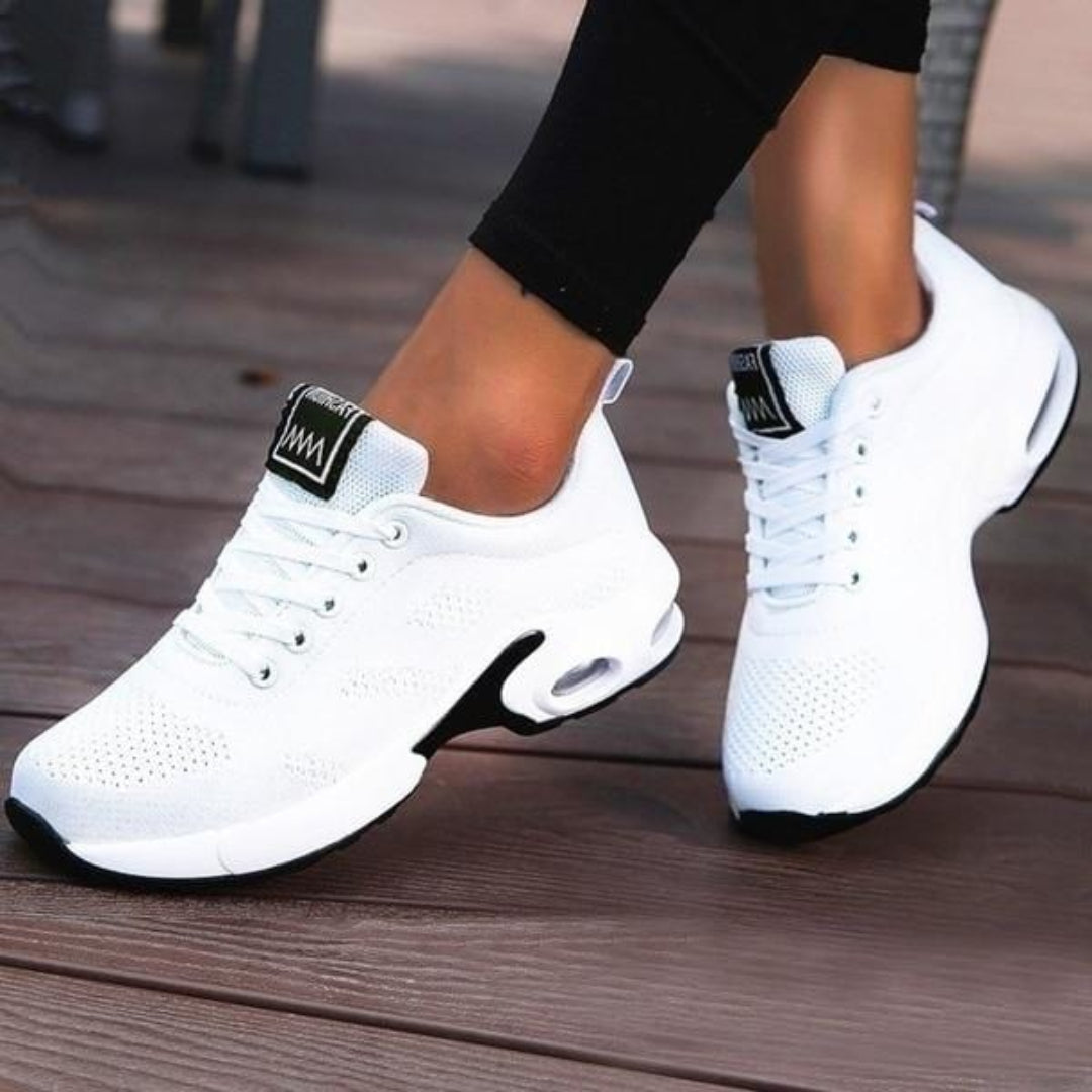 Baskets basses pour femme de couleur blanche avec semelle épaisse et détails noirs, portées avec un legging noir, offrant un design moderne, léger et respirant, adaptées à un usage quotidien et à la marche.