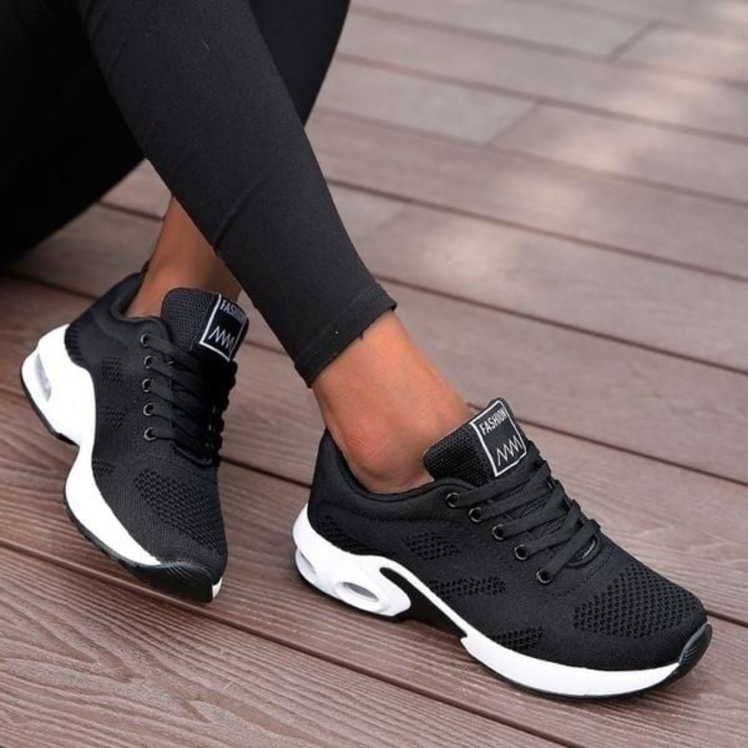 Chaussures de sport basses pour femme, de couleur noire avec semelle blanche épaisse, portées avec un legging noir, au design moderne et respirant, idéales pour un usage quotidien.