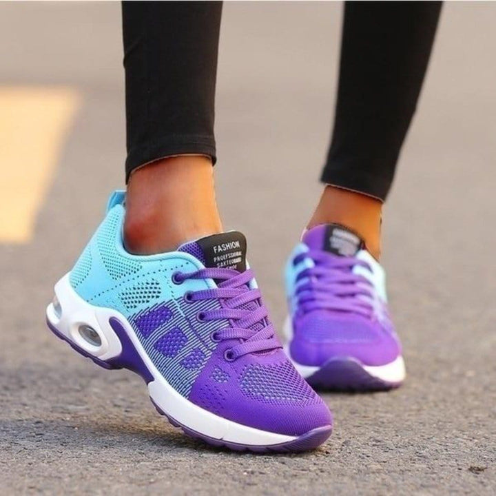 Baskets basses pour femme aux couleurs violet et bleu clair avec semelle blanche épaisse et zones amortissantes visibles, portées avec un legging noir, au design moderne, respirant et confortable, idéales pour la marche et un usage quotidien.