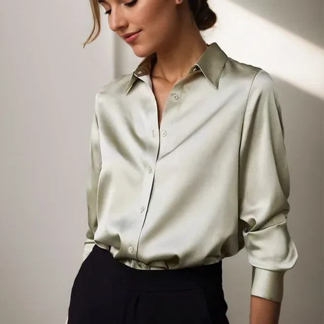 Femme portant une blouse fluide vert clair au style tendance, avec col chemise, fermeture boutonnée et manches longues aux poignets ajustés, associée à un pantalon taille haute pour une allure élégante et professionnelle.