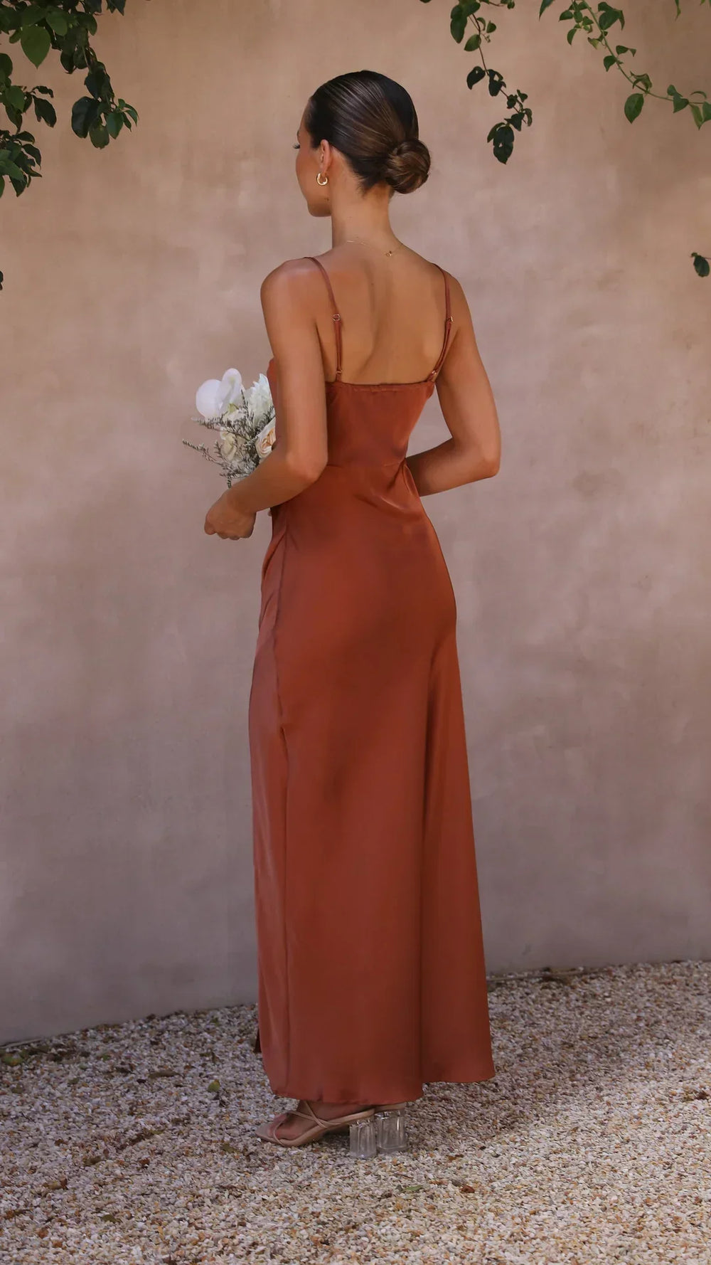 Vue arrière de la robe maxi Leona pour femme, avec des bretelles spaghetti fines et une coupe fluide. La robe, d'une teinte brune élégante, épouse parfaitement la silhouette et offre un look moderne et raffiné. Idéale pour des événements estivaux ou des occasions spéciales, elle combine confort et sophistication.
