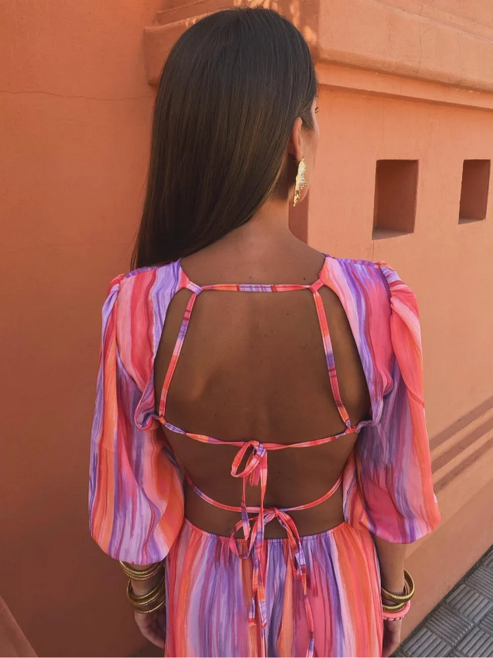 Vue arrière de la robe avec des découpes au dos et des liens à nouer, mettant en valeur le design élégant et contemporain. Les motifs tie-dye vibrants dans des tons de rose, violet et orange ajoutent une touche dynamique à ce modèle audacieux.