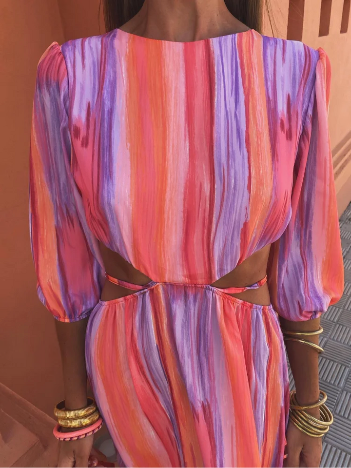 Gros plan sur la partie supérieure de la robe aux motifs tie-dye vibrants, avec des découpes élégantes sur les côtés. La robe présente un dégradé de couleurs roses, violets et oranges, souligné par des accessoires dorés, créant un look tendance et moderne.