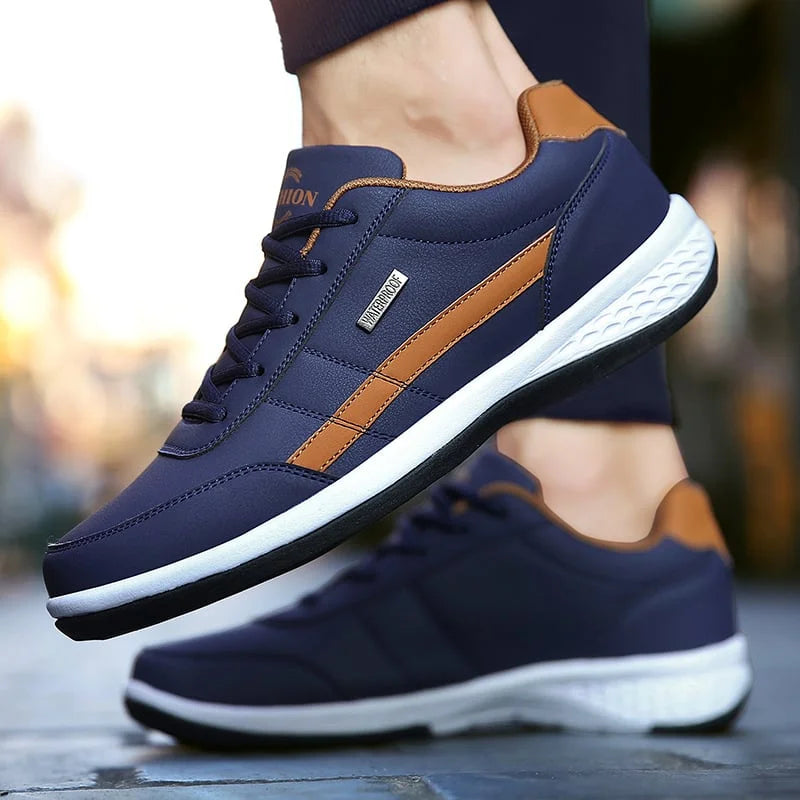 Gros plan sur la chaussure décontractée homme Loïc moderne, basket bleu marine avec bande camel, lacets assortis et semelle blanche amortissante, portée en extérieur.