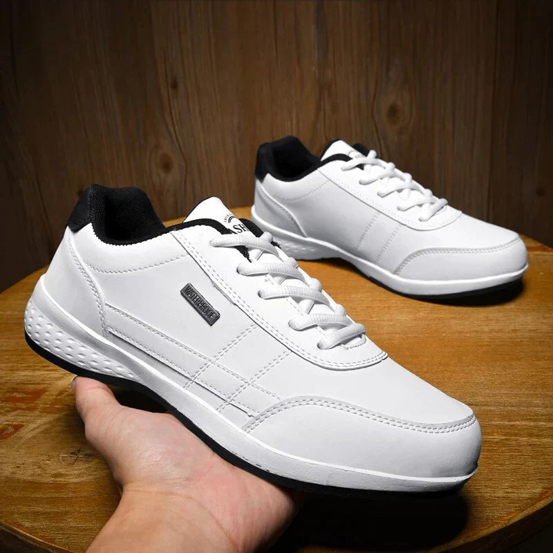 Chaussures décontractées pour homme Loïc modernes, baskets blanches avec col noir, lacets blancs et semelle antidérapante, présentées sur table en bois avec une paire en arrière-plan.