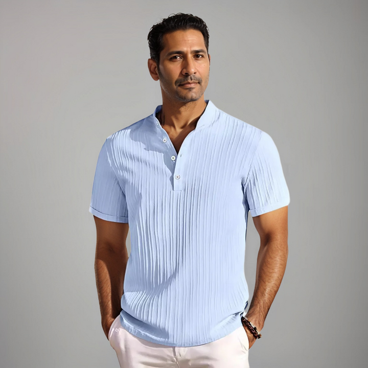 Homme portant un polo bleu clair à manches courtes avec un col à boutons et un motif rayé subtil. Un modèle moderne et élégant, idéal pour un look estival frais et raffiné.
