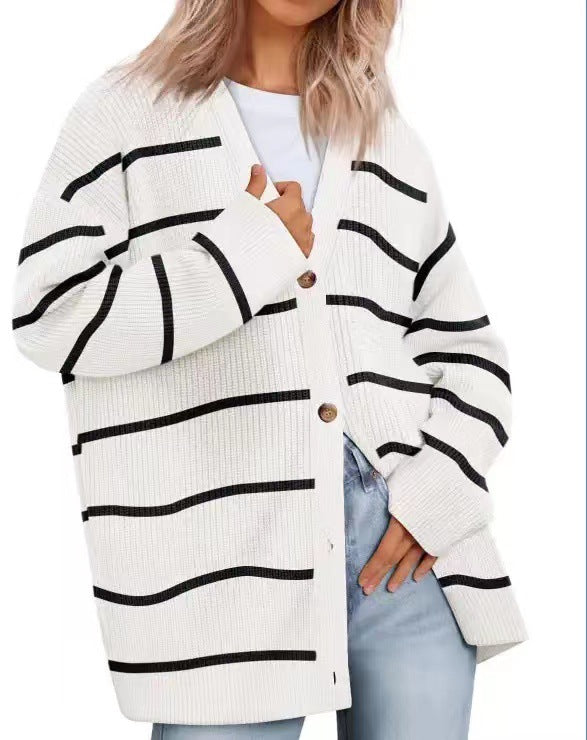 Femme portant un cardigan blanc à col en V avec des rayures noires, doté de boutons en bois et d’une coupe oversize. Le vêtement est superposé à un t-shirt blanc et associé à un jean, offrant un style moderne, décontracté et tendance.