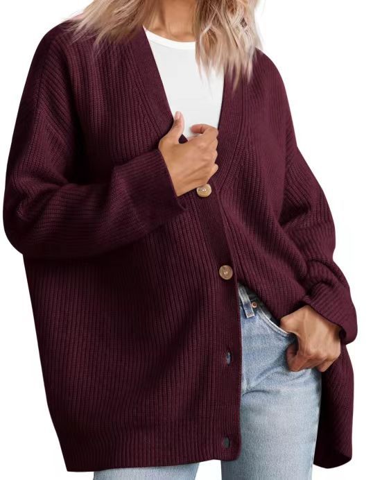 Une femme porte un cardigan Rot à col en V, orné de gros boutons en bois et à la coupe ample. Ce vêtement est superposé à un t-shirt blanc et associé à un jean, créant ainsi un look moderne, confortable et décontracté.