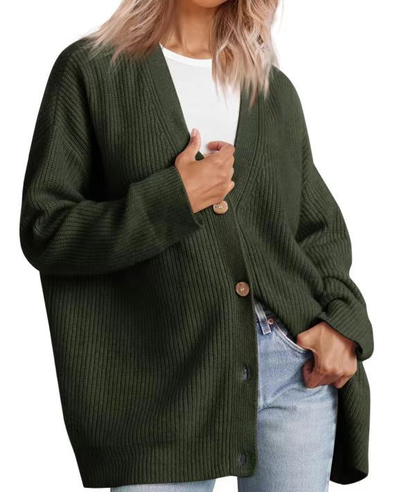 Femme portant un cardigan vert foncé à col en V, doté de gros boutons en bois et d’une coupe oversize. Le vêtement est superposé à un t-shirt blanc et associé à un jean clair, créant un style moderne, confortable et décontracté.
