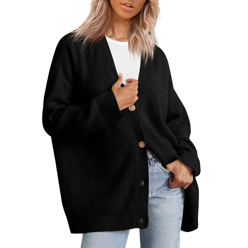 Femme portant un cardigan noir à col en V, doté de gros boutons en bois et d’une coupe oversize. Le vêtement est superposé à un t-shirt blanc et associé à un jean clair, offrant un style moderne, décontracté et confortable.