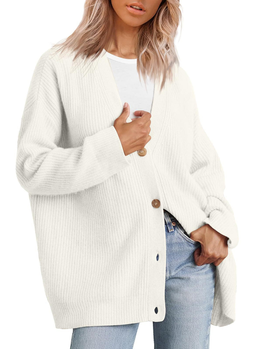 Femme portant un cardigan blanc à col en V, doté de gros boutons en bois et d’une coupe oversize. Le vêtement est superposé à un t-shirt blanc et associé à un jean clair, offrant un style moderne, minimaliste et décontracté.