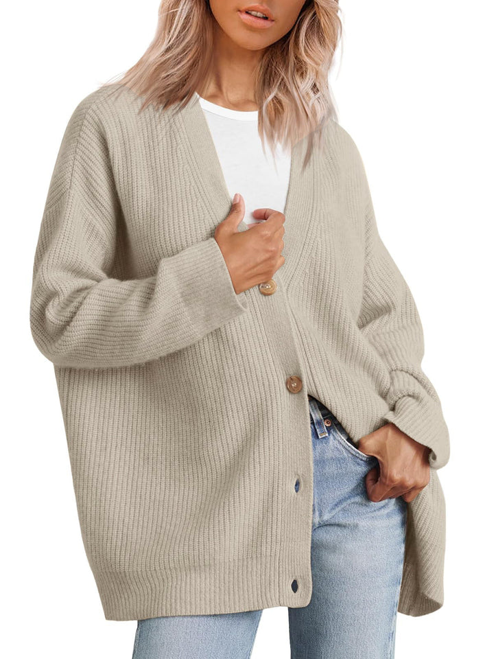 Femme portant un cardigan beige sable à col en V, doté de gros boutons en bois et d’une coupe oversize. Le vêtement est superposé à un t-shirt blanc et associé à un jean clair, offrant un style moderne, décontracté et confortable.