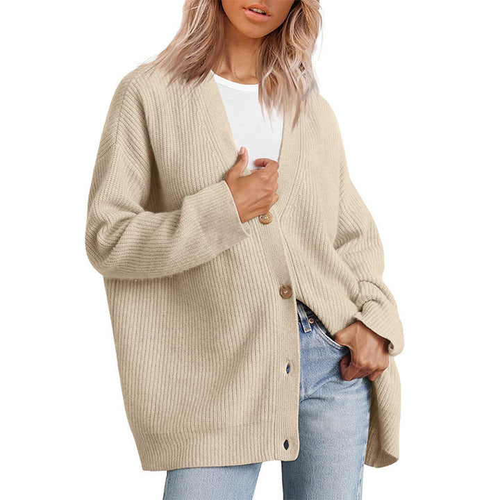 Femme portant un cardigan beige clair à col en V, doté de gros boutons en bois et d’une coupe oversize. Le vêtement est superposé à un t-shirt blanc et associé à un jean clair, créant un style moderne, décontracté et confortable.