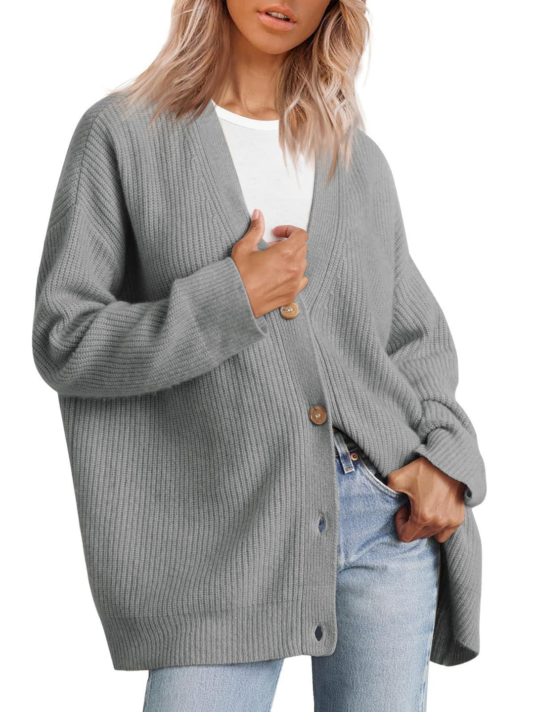 Femme portant un cardigan gris à col en V, doté de gros boutons en bois et d’une coupe oversize. Le vêtement est superposé à un t-shirt blanc et associé à un jean clair, offrant un style moderne, décontracté et confortable.