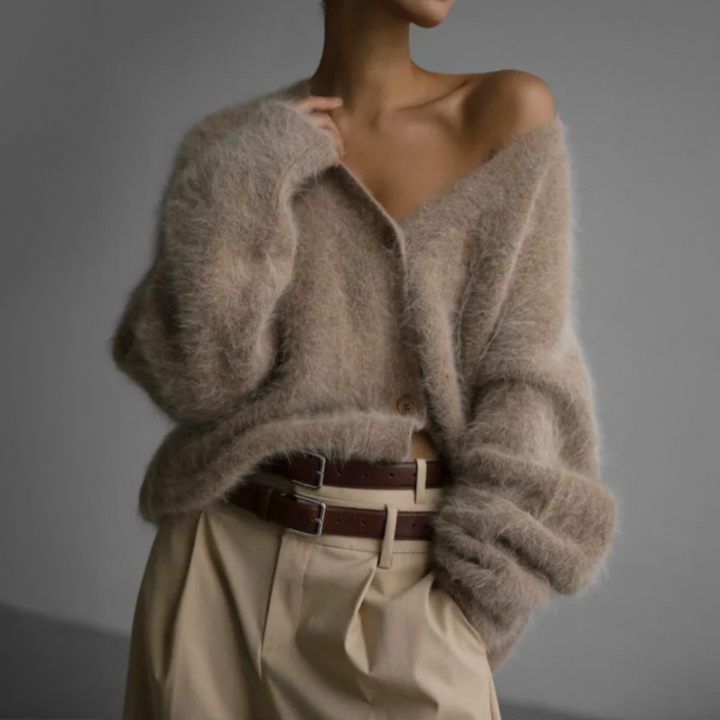 Femme portant un cardigan ample et duveteux de couleur beige chaud, légèrement tombant sur l’épaule, associé à un pantalon beige taille haute avec ceinture double en cuir marron. L’ensemble dégage une allure décontractée, féminine et raffinée, parfaite pour un style automnal élégant et confortable.