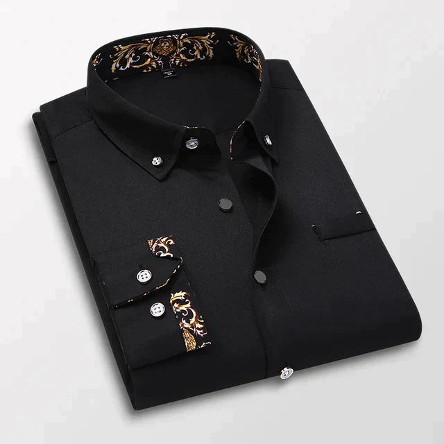 Chemise longue pour hommes Ludovic moderne noire, pliée avec col boutonné et détails baroques dorés à l’intérieur du col et sur les poignets, présentée sur fond clair.