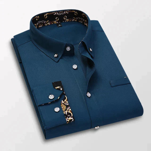 Chemise longue pour hommes Ludovic moderne bleu marine, pliée avec col boutonné et détails baroques dorés à l’intérieur du col et sur les poignets, présentée sur fond clair.