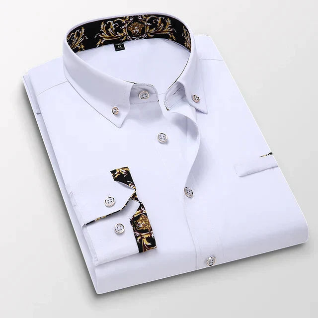 Chemise longue pour hommes Ludovic moderne blanche, pliée avec col boutonné et détails baroques dorés à l’intérieur du col et sur les poignets, présentée sur fond clair.