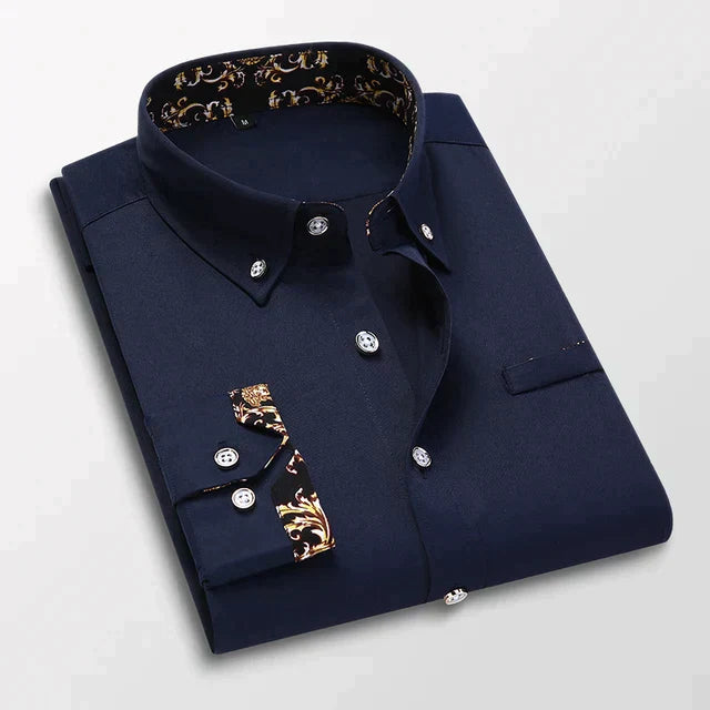 Chemise longue pour hommes Ludovic moderne bleu nuit, pliée avec col boutonné et détails baroques dorés à l’intérieur du col et sur les poignets, présentée sur fond clair.