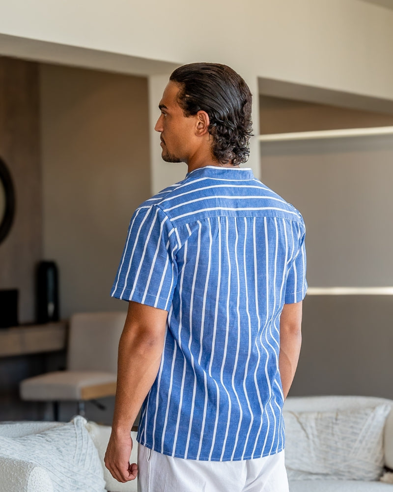 Homme portant la chemise d’été moderne Lyam en lin bleu à rayures blanches, vue de dos dans un intérieur élégant, avec coupe légère et manches courtes pour un style estival raffiné.