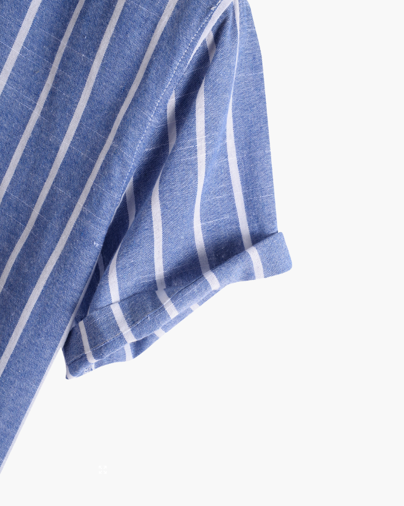 Gros plan sur la manche retroussée de la chemise d’été moderne Lyam en lin bleu à rayures blanches, mettant en valeur le tissu léger et la finition élégante.