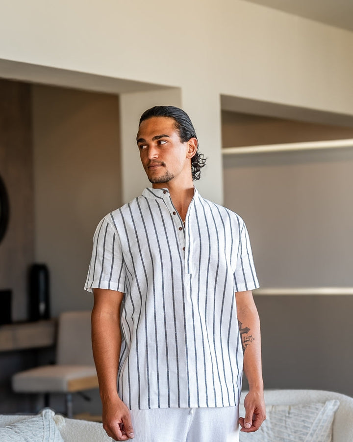 Homme portant la chemise d’été moderne Lyam en lin blanc à rayures verticales foncées, avec col officier et manches courtes, pour un style élégant et décontracté en été.